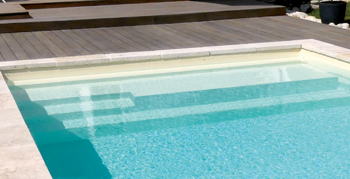 La piscine coque à fond plat avec banquette et repose coude et repose pieds