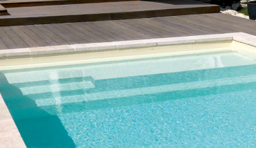 La piscine coque à fond plat avec banquette et repose coude et repose pieds