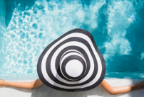 Une jeune femme avec un grand chapeau se détend au bord d'une piscine